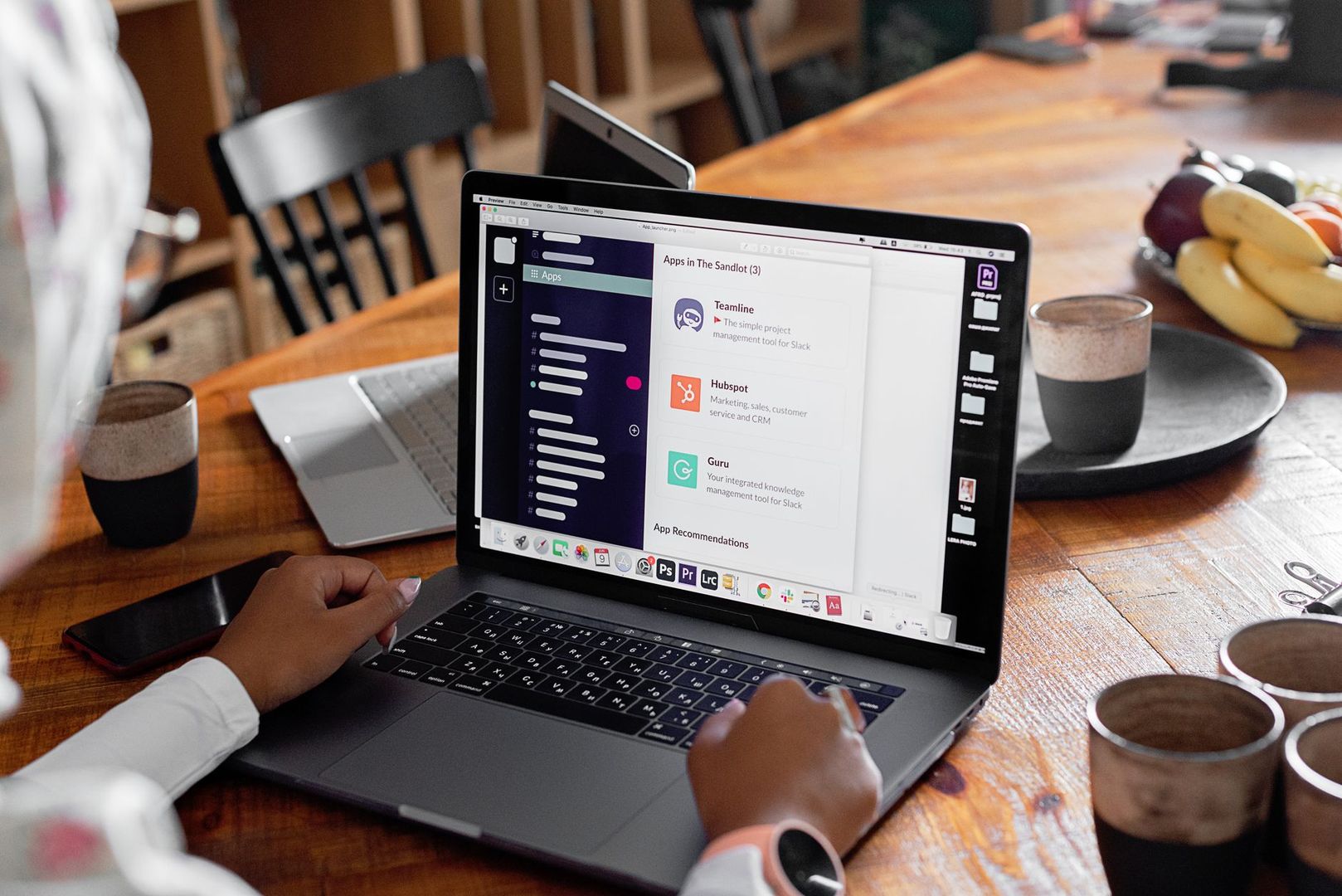 A person using a laptop displaying integrated productivity apps at a wooden table.